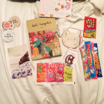 A photograph of Doll Hospital Issue One with a selection of sweets, Doll Hospital stickers, cat cards, and a mix tape laid across a bed sheet
